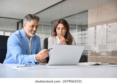 Business team of two busy professionals working together using laptop looking at computer. Male executive manager explaining corporate project online strategy to female partner sitting at office desk. - Powered by Shutterstock
