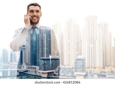 Business, Technology, Communication And People Concept - Young Smiling Businessman Calling On Smartphone Over Dubai City Background With Double Exposure Effect