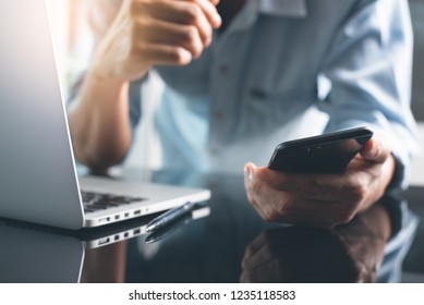 Business And Technology Concept. Pensive Casual Business Man, Freelancer, Programmer Using Smart Mobile Phone While Working On Laptop Computer Thinking About His Project In Modern Office, Close Up