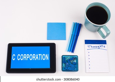 Business Term / Business Phrase On Tablet PC - Blue Colors, Coffee, Pens, Paper Clips And Note Pads On White - White Word(s) On Blue - C Corporation