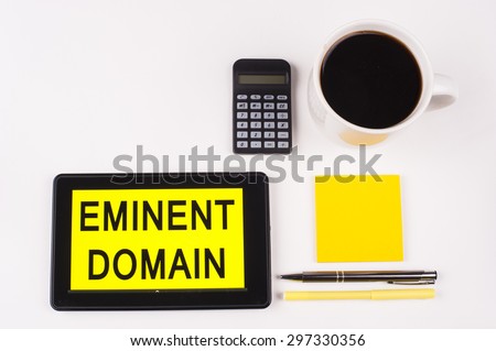 Business Term / Business Phrase on Tablet PC with a cup of coffee, Pens, Calculator, and yellow note pad on a White Background - Black Word(s) on a yellow background - Eminent Domain