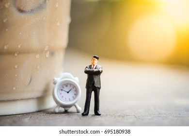 Business, Time And Coffee Concept. Businessman Miniature Figures Standing And Thinking On Wooden Table With A Plastic Cup Of Take Away Iced Coffee And Mini Clock Toy.