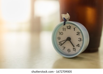 Business, Time And Relax Concept. Businessman Miniature Figure People Sitting And Reading A Newspaper O Round Clock With Takeaway Plastic Cup Of Iced Black Coffee On Wooden Table With Copy Space.