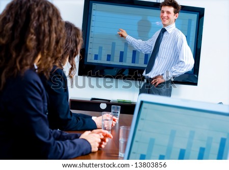 Business training at office, happy businessman presenting successful financial numbers on screen of plasma TV at meeting room, smiling.