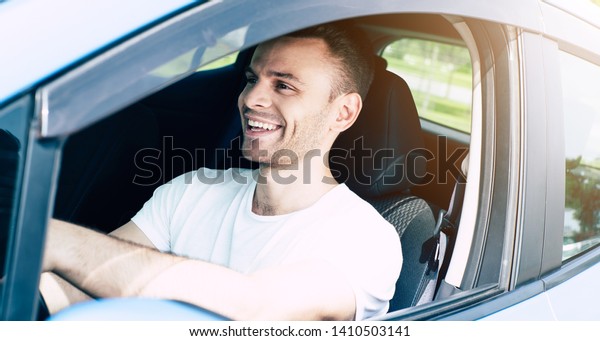 Business travel. Happy handsome young man driving\
his car and smiling. Excited driver in urban city. Electro car,\
vehicle of future.