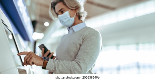 Business Traveler Making Check In On Self Service Machine At Airport. Businessman Wearing Protective Face Mask Checking In With Automatic Machine At Airport Terminal.