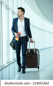 Business Traveler Pulling Suitcase And Holding Passport And Airline Ticket