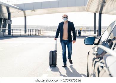 Business Traveler Pulls Suitcase From Modern Airport Terminal, Walks To Car, Wears Medical Disposable Mask On Face, Prevents From Coronavirus During Dangerous Pandemic Situation. Full Length Shot