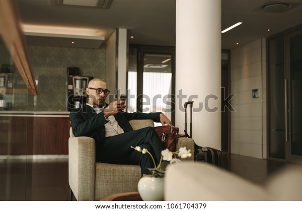 Business\
traveler waiting in airport lounge and using mobile phone.\
Businessman waiting for fight at airport\
lounge.