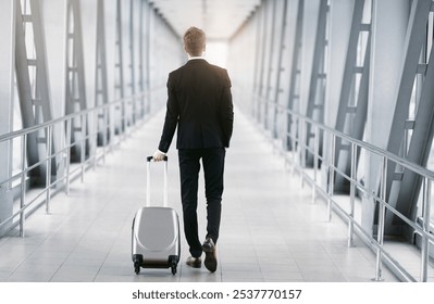 Business Trip Concept. Back view of classy guy in suit pulling trolley bag walking out the airport, free space - Powered by Shutterstock