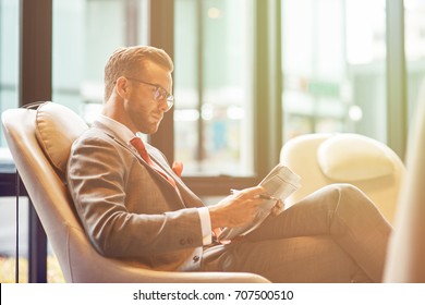 Business trip. Confident professional businessman sitting in the departure lounge and reading a newspaper while waiting for his flight - Powered by Shutterstock