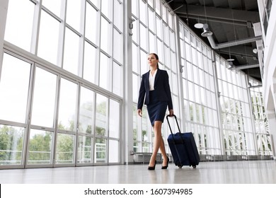 Business Trip, Corporate And People Concept - Young Businesswoman Walking With Travel Bag Along Office Building Or Airport