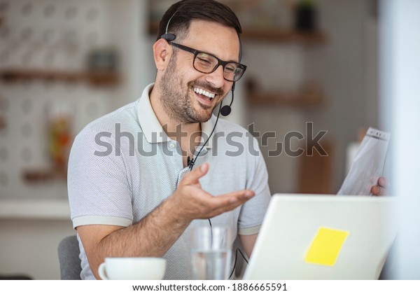 Business Video Conference. Smiling man in\
eyeglasses holding paper documents, chatting online with clients on\
laptop at workplace. Smiling biracial businessman holding video\
call with clients\
partners