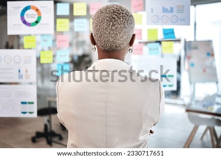 Business woman, back and thinking in project management, marketing or planning at the office. Rear view of Female person, manager or employee checking vision board of company statistics at workplace
