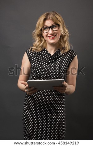 Business woman blond smiling in glasses holding tablet pc notebook studying on black background. Emotional face, red lips.