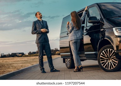 Business Woman And Businessman Stay Near Vip Van. Couple Get In Luxury Transfer Car