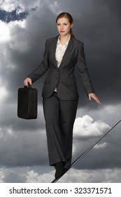 Business woman with case balancing on rope.
