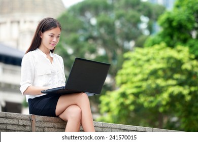 Business Woman With Computer Laptop Working Outside Looking At Screen In Business District, Central, Hong Kong. Young Female Professional Businesswoman Sitting Outdoors. Asian Chinese Caucasian Woman.