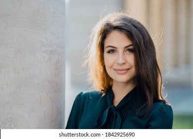 business woman confident smart teacher management student brunette of European appearance standing on the street smiling in a green dress and looking at the camera. Sunny day business center
