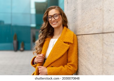 Business woman dressed yellow coat standing outdoors corporative building background Caucasian female business person eyeglasses on city street near office building with windows Stylish businesswoman