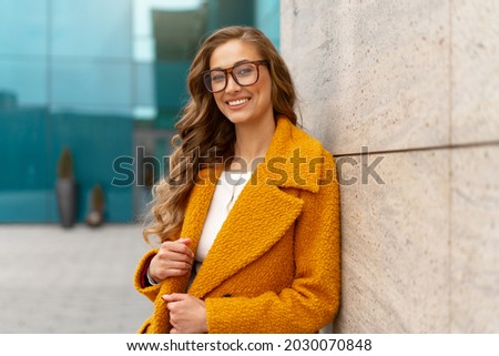 Business woman dressed yellow coat standing outdoors corporative building background Caucasian female business person eyeglasses on city street near office building with windows Stylish businesswoman