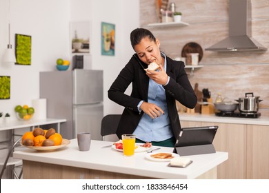 Business woman eating toasted bread with butter while working on laptop during breakfast. Concentrated business woman in the morning multitasking in the kitchen before going to the office, stressful
