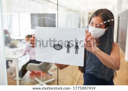 Business woman with everyday mask fastens notice board with rules of conduct against infection with Covid-19