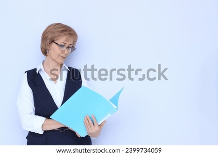 A business woman in glasses looks carefully and intently at documents in a folder, a working moment in the office, a team leader is studying a contract, a light neutral background with space for text