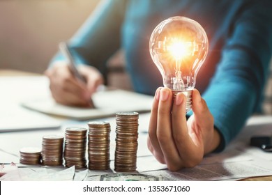 Geschäftsfrau Hand, die eine Glühbirne mit Münzen auf dem Schreibtisch hält. Konzeptsparen von Energie und Geld