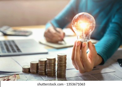 Business Woman Hand Holding Lightbulb With Coins Stack On Desk. Concept Saving Energy And Money