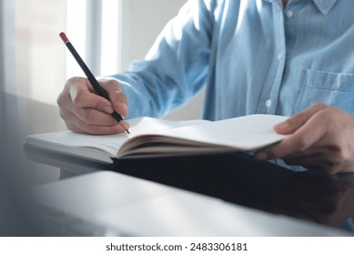 Business woman hand writing with pencil planning event on notebook. Job schedule, event planning, to do list and reminder, E-learning. Woman working on laptop and taking note on office desk, close up - Powered by Shutterstock