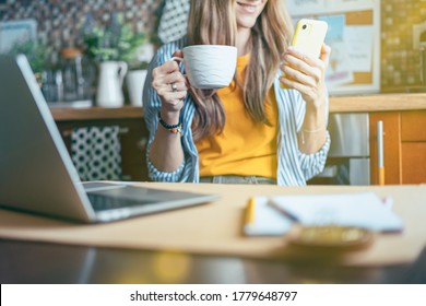 Business Woman Having A Facetime Video Call. Happy And Smiling Girl Working From Home Office Kithcen And Drinking Coffee. Using Computer And Mobile Phone. Distance Learning Online Education And Work. 