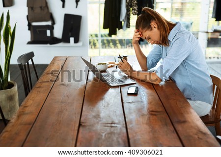 Business Woman Having Headache While Working Using Laptop Computer. Stressed And Depressed Girl Touching Her Head, Feeling Pain While Sitting At Wooden Table At Cafe. Work Failure Concept