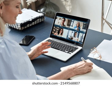 Business Woman Having Virtual Team Meeting On Video Conference Call Using Laptop Computer. Social Distance Work From Home Office With Diverse People Group In Remote Online Chat. Over Shoulder View