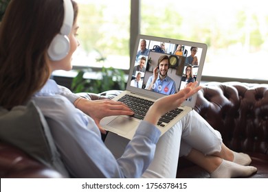Business woman in headphones lying on sofa speak talk on video call with colleagues on online briefing during self isolation and quarantine. Webcam group conference with coworkers on laptop at office.