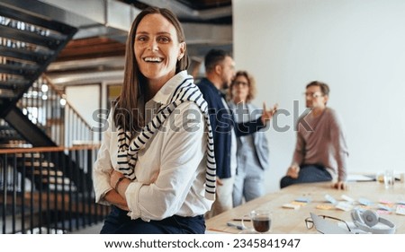 Business woman in her 30's looking at the camera in a boardroom. Business woman having a meeting with her team in an office. Female professional working on a project with her colleagues.