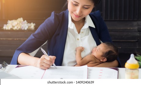 Business Woman Holding Baby In Her Arms While Working, Signing Contract. Single Asian Mum Taking Care Of Newborn In The Office. Can Use For Varieties Of Concepts. 