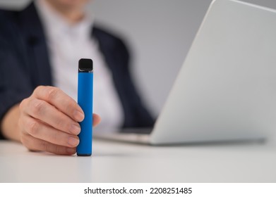 Business woman holding disposable vape while sitting at laptop.  - Powered by Shutterstock