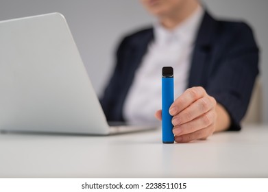 Business woman holding disposable vape while sitting at laptop.  - Powered by Shutterstock