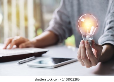 Business woman holding light bulb on the desk in office and using  computer in  financial,accounting,energy,idea concept.