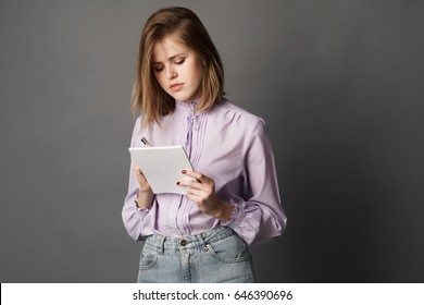 Business Woman Holds A Notebook With A Pen. Something Writes And Thinks. Studio Photography. One On A Gray Background