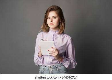 Business Woman Holds A Notebook With A Pen. Something Writes And Thinks. Studio Photography. One On A Gray Background