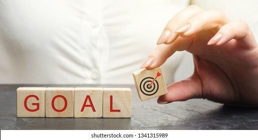 Business Woman Holds Wooden Blocks With The Word Goal. The Concept Of Achieving Business Goals. Reaching New Heights. Execution Of A Business Plan. Purposefulness. Perseverance. Target. Planning