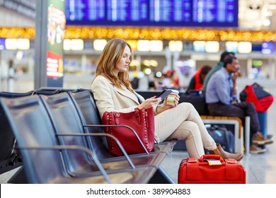 Business Woman At International Airport Reading Book And Drinking Coffee In Terminal. Angry Passenger Waiting. Canceled Flight Due To Pilot Strike.