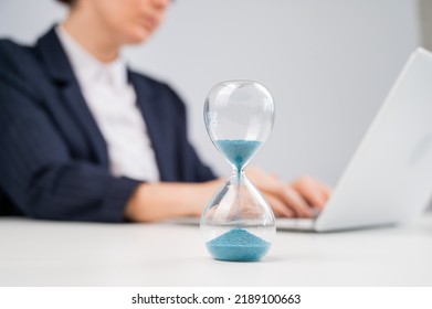 Business woman keeps track of time on an hourglass while working.