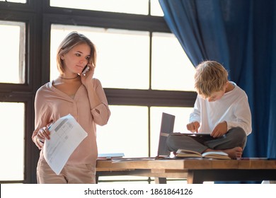 Business Woman With Laptop And Son With Tablet. Multi Tasking, Freelance And Motherhood Concept Working At Home As Her Cute Little Boy Plays On A Tablet Alongside Her As She Works