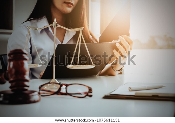 Business woman and lawyers\
discussing contract papers with brass scale on wooden desk in\
office. Law, legal services, advice, Justice and real estate\
concept.