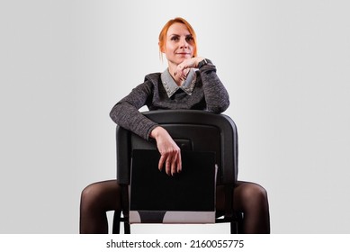 Business Woman, Legs Wide Apart, Sits On A Chair Backwards, On A Gray Background. High Quality Photo