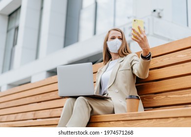 Business Woman In Medical Protective Face Mask Taking A Selfie On Cellphone And Working At Laptop Sit Down On Bench Outside. Happy Student Lady Girl With Phone Distance Learning And Online Education.