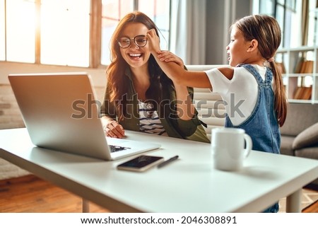 Business woman and mom are trying to work on a laptop when her little daughter is playing and interrupts her. Freelance, work from home.